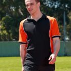 Man in a black and orange shirt walking on a track outdoors.