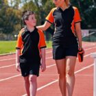 A woman and boy in matching sportswear walk on a track, chatting and smiling.