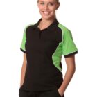 Smiling person in a black and green polo shirt with hands in pockets against a white background.