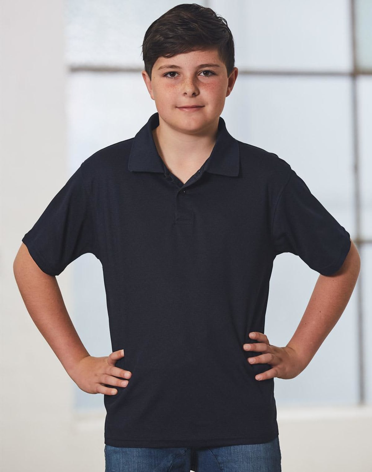 Boy in a navy polo shirt and jeans stands with hands on hips, looking confident.
