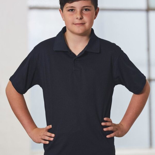 A young boy in a dark polo shirt stands with hands on hips, neutral expression.