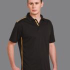 Man wearing a black polo shirt with yellow stripes, standing against a gray background.