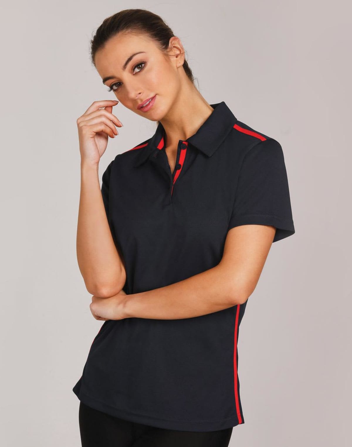 Person in a black and red collared shirt posing with hand to chin, against a plain background.