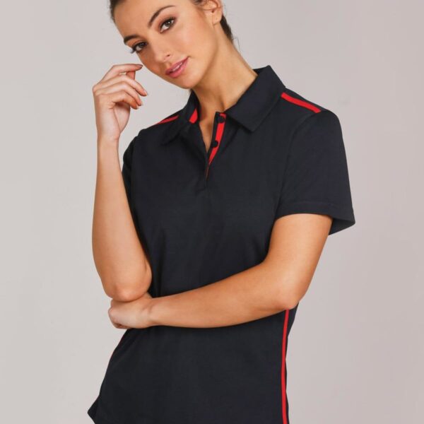 Woman in a black polo shirt with red stripes, posing thoughtfully against a gray background.