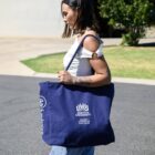 Woman walking outside carrying a large blue Griffith University tote bag.