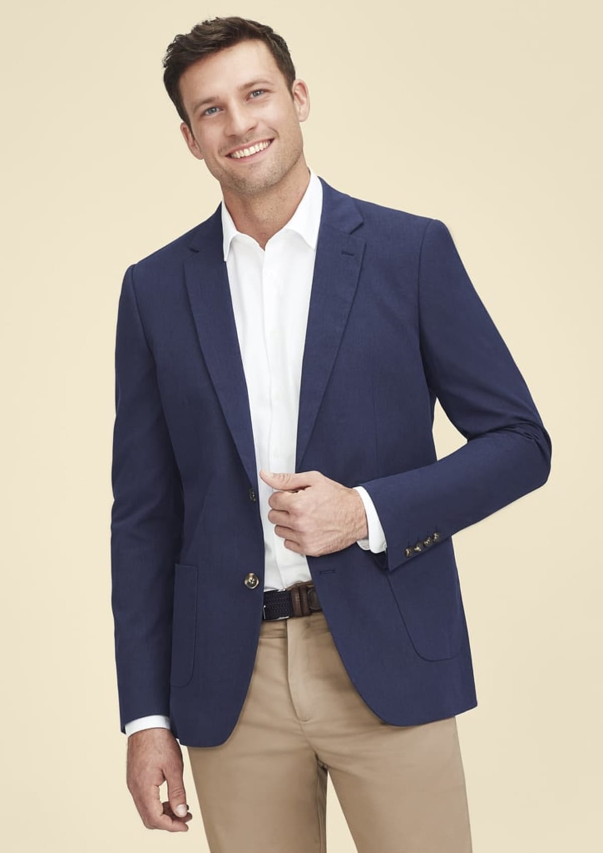 Man in blue blazer and khaki pants smiling against a beige background.