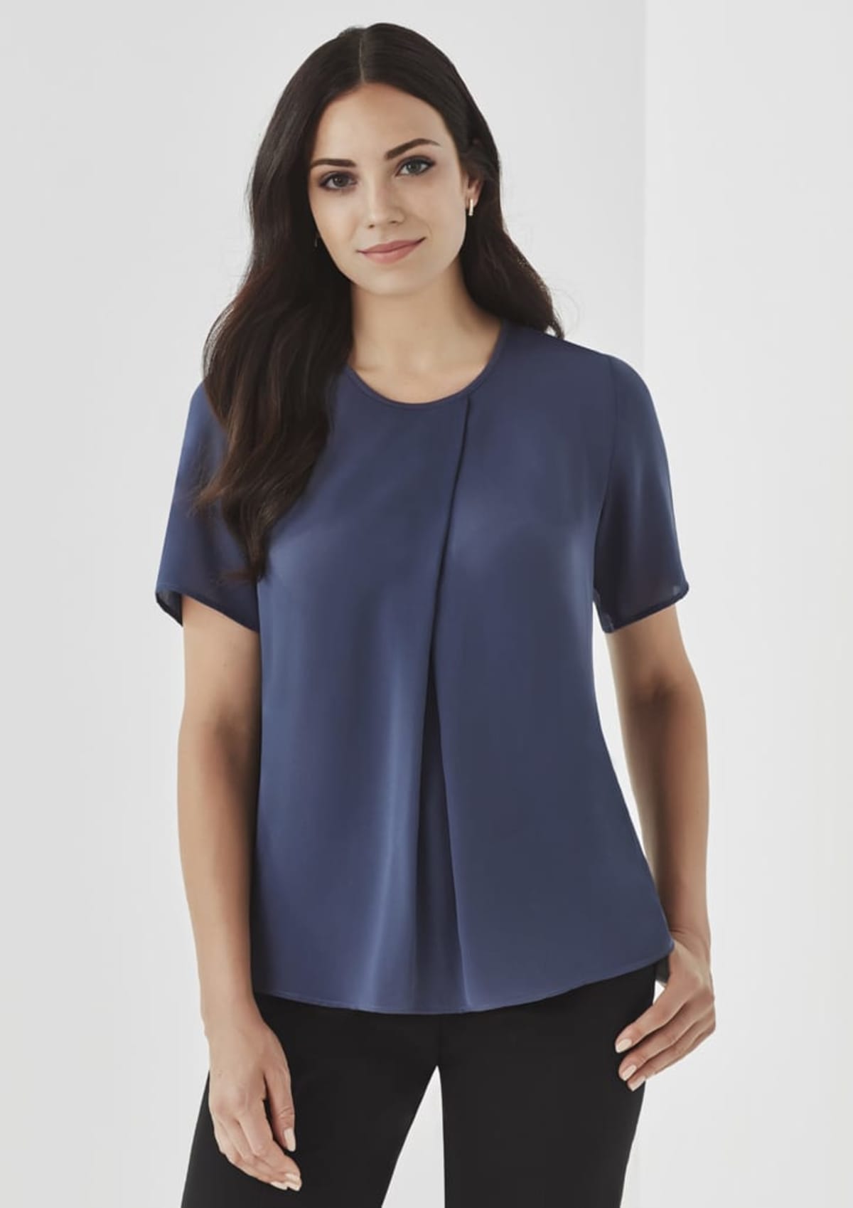 Woman wearing a short-sleeve navy blouse and black pants, standing against a plain background.