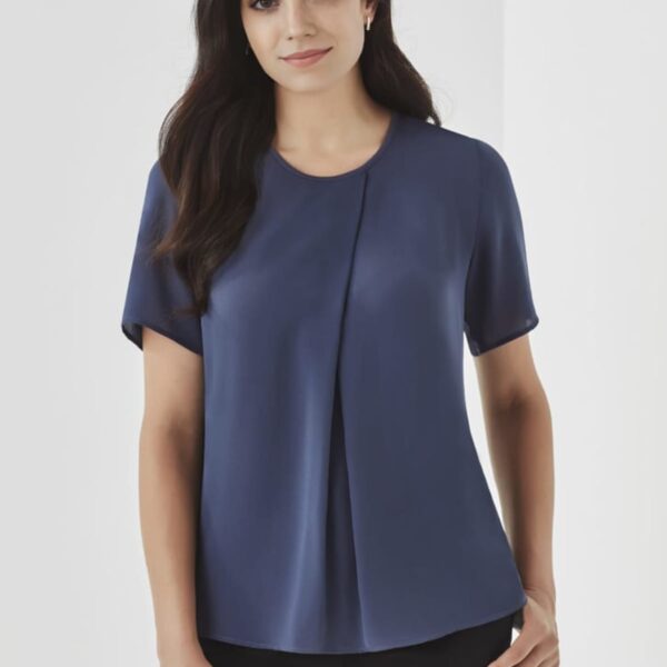 Woman with long dark hair wearing a short-sleeve navy blouse and black pants, standing.