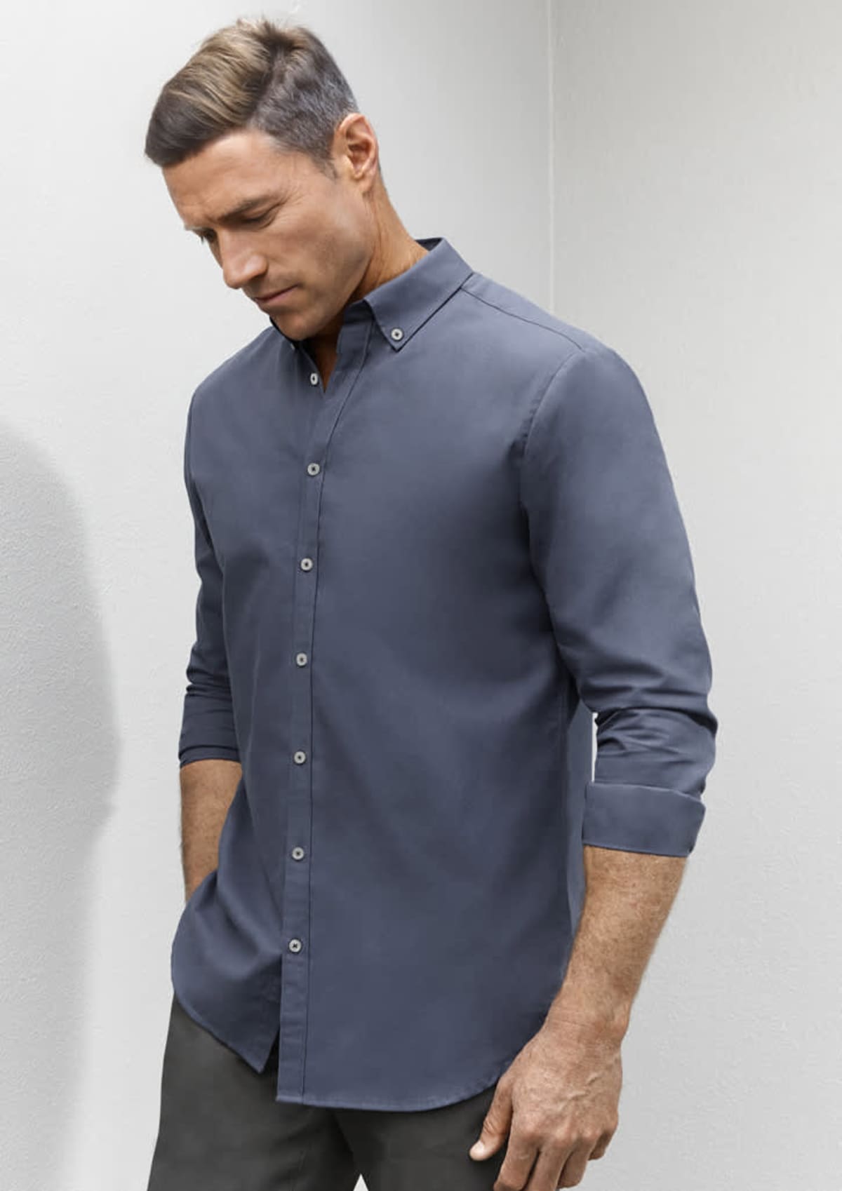 Man wearing a long-sleeve, button-up gray shirt with sleeves rolled up, looking down.
