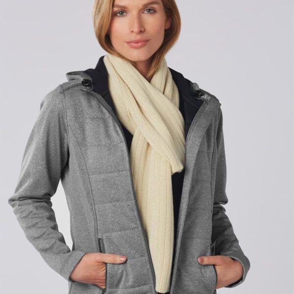 Person in a gray jacket and cream scarf standing against a plain background.