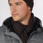 Man in a gray jacket, brown scarf, and hat looks to the side.