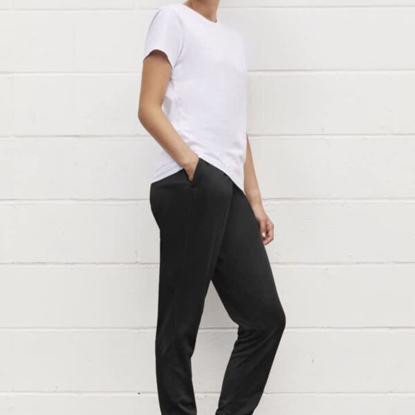 Person wearing a white T-shirt, black joggers, and sneakers, leaning against a white wall.