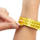 Hand placing a gold wristband on a wrist.