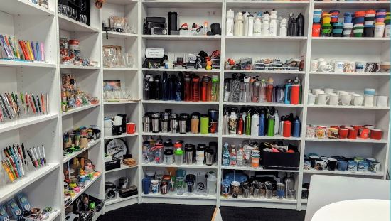 Shelves filled with wholesale promotional products like mugs, bottles, and office supplies.