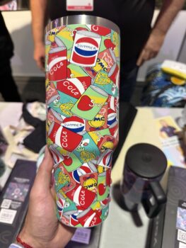 Hand holds a tumbler with colorful APPA 2025 summer-themed soda can illustrations and doodles.