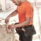 Person in orange shirt measuring wood at a construction site.