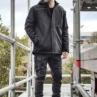 Man in black winter clothes stands on scaffolding outdoors.