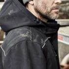 Person in a gray beanie and black jacket with a hood, looking to the side.