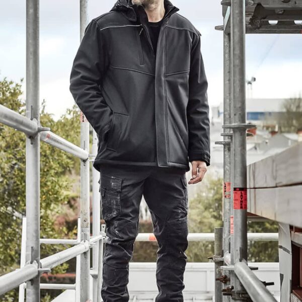 Person in workwear and beanie standing on scaffolding outdoors.