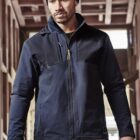 Man in a blue jacket and beanie stands in a wooden structure.
