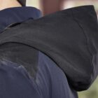 Person wearing a dark jacket with hood and beanie, shown from behind.