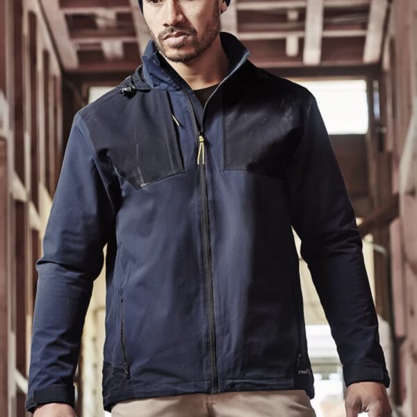 Man in a navy jacket and beanie in a wooden construction site.