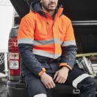Man in orange jacket and beanie sitting on a truck tailgate, looking thoughtful.