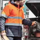 Construction worker in orange jacket holding a level, reaching into a truck bed.