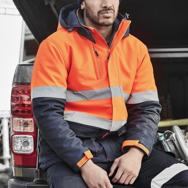 Man in orange reflective jacket sitting on a vehicles open tailgate, looking thoughtful.