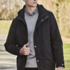 Person in a black jacket and beanie walking outdoors on a sunny day.