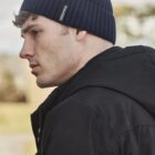 Man in a black jacket and navy beanie looking sideways.