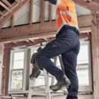 Worker in orange safety shirt on ladder, working on unfinished wooden ceiling.