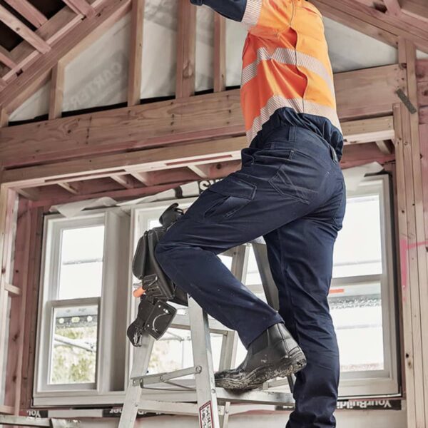 Worker on ladder in partially constructed room, wearing safety gear and reaching up.