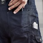 Close-up of person wearing navy work pants with a phone and measuring tape in the back pocket.