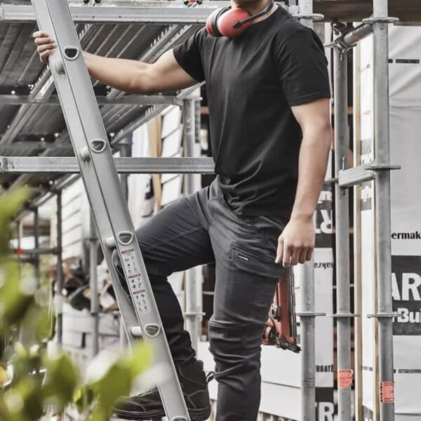 Man in black clothing standing on a ladder at a construction site with headphones around his neck.