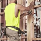 Builder in yellow tank top measures timber framework with a tape measure.