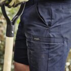 Person in blue shorts holding a shovel, wearing green gardening gloves.