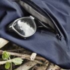 Sunglasses partially in zippered pocket on navy fabric, placed on intertwined branches.