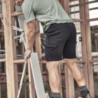 Person in t-shirt and shorts sweeping sawdust at a construction site.