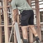 Man in a green shirt mopping a wooden floor in a building under construction.