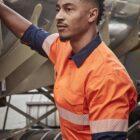 Man in orange safety jacket standing by industrial equipment.