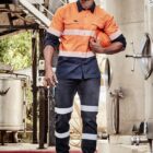 Man in high-visibility workwear holds a helmet in an industrial setting.