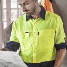 Man in high-vis workwear examining architectural plans indoors.