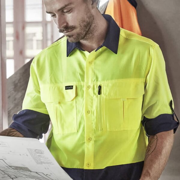 Person in a yellow high-vis shirt looking at construction plans indoors.