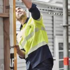 Builder measuring a wall with a level tool at a construction site.