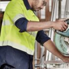 Worker in yellow safety gear uses a circular saw in a workshop.