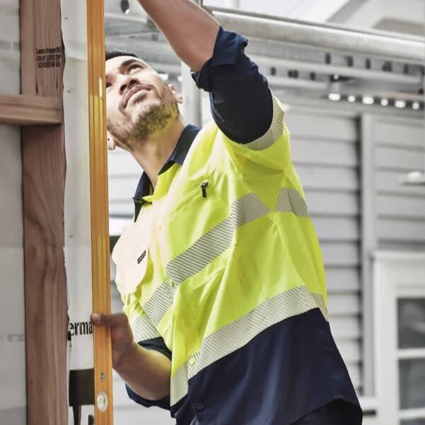 A construction worker in a safety vest measures wood on a building site.