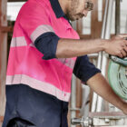Person cutting wood with a saw, wearing safety gear, including ear protection and goggles.