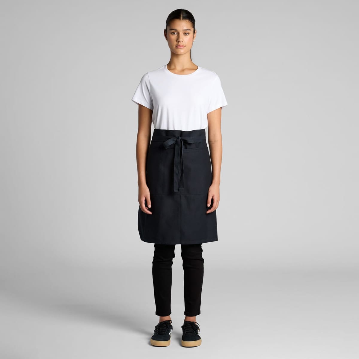 Person wearing a white t-shirt, black apron, black pants, and black shoes standing facing forward.