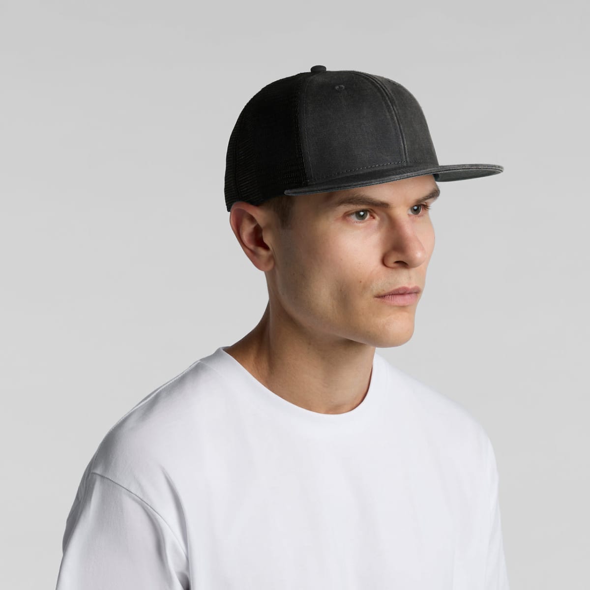 Man in a white shirt and black baseball cap looking to the side against a plain background.